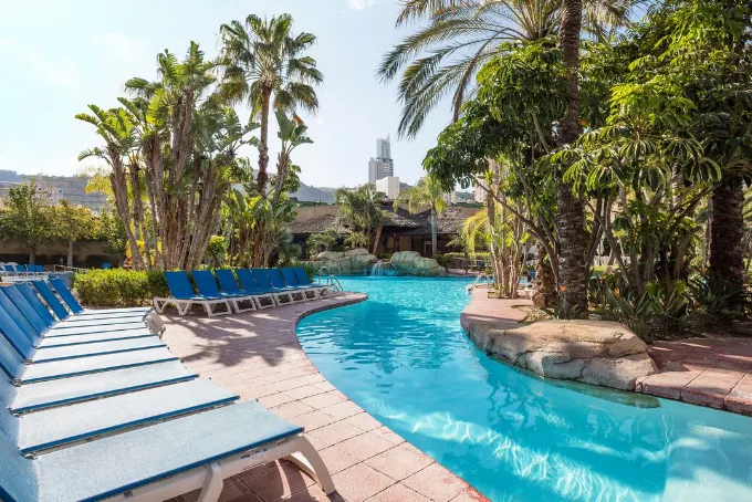 Curved lagoon pool with sun loungers, waterfalls and tropical palms at Meliá Benidorm